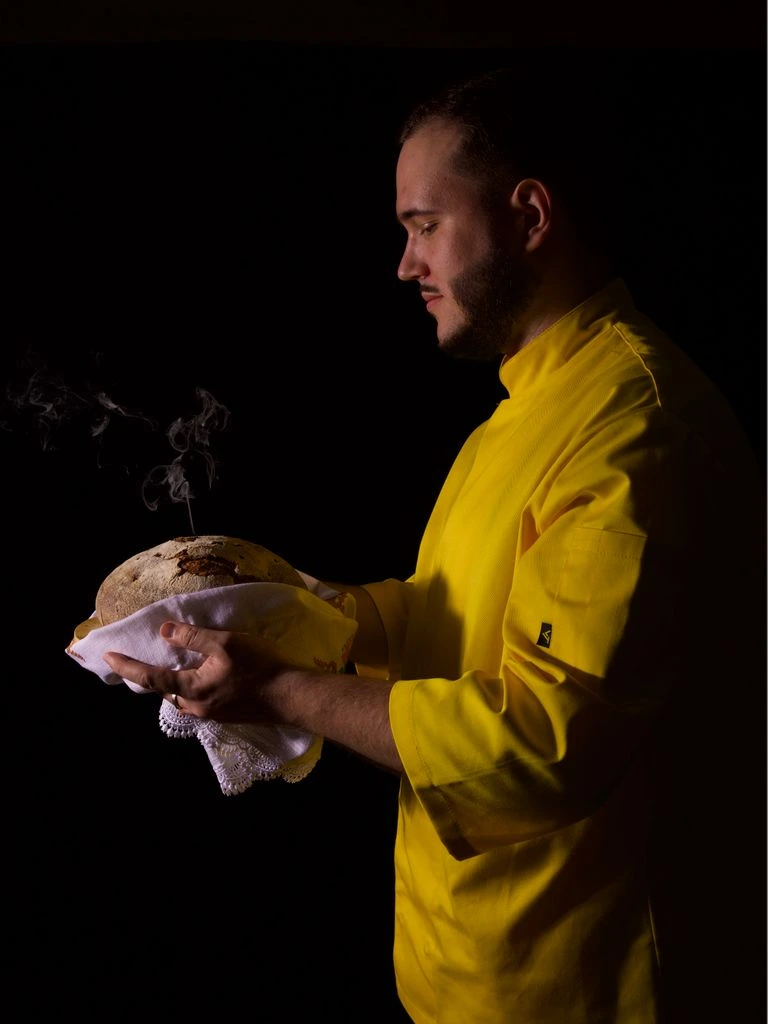 Portrait of the head chef, photographed beside the wood-fired stone hearth.